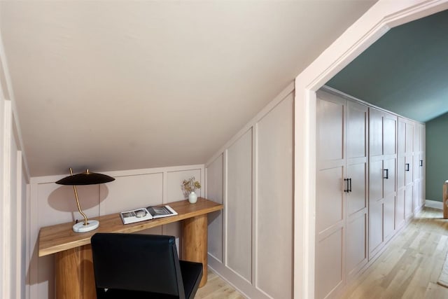 office area with lofted ceiling, light wood-style flooring, and a decorative wall