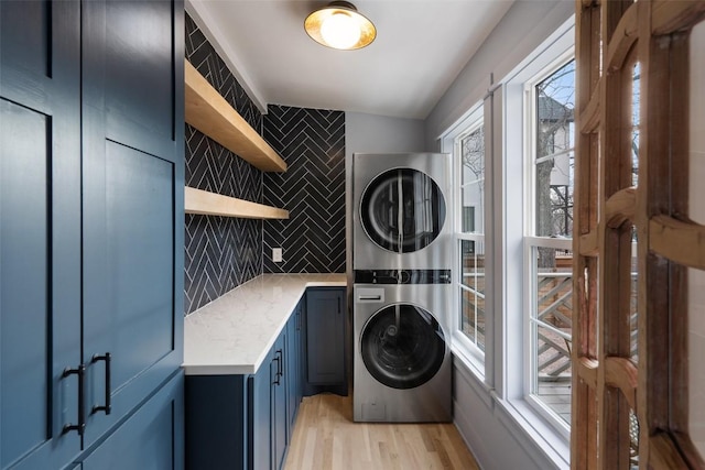 laundry room featuring cabinet space, light wood-style flooring, and stacked washing maching and dryer