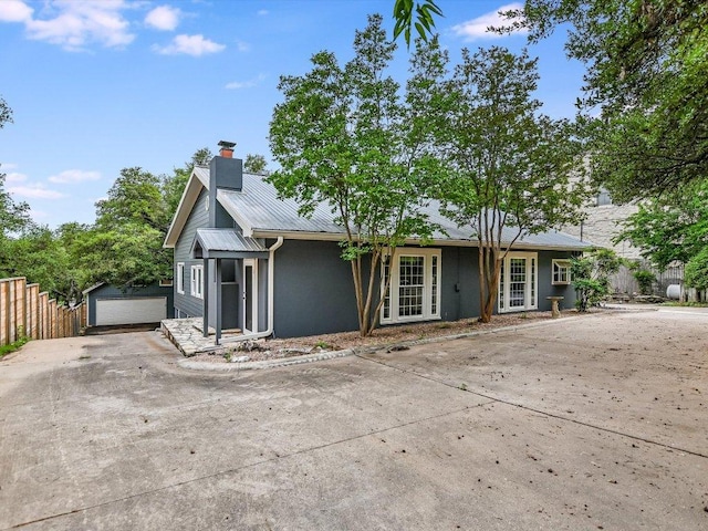 view of front of home featuring a chimney, metal roof, fence, driveway, and an outdoor structure