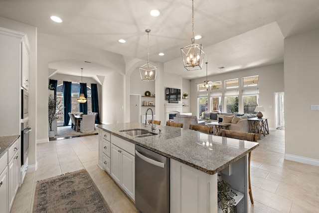 kitchen with white cabinets, appliances with stainless steel finishes, a kitchen island with sink, a fireplace, and a sink