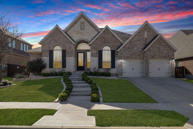 french country inspired facade with a garage, a front yard, concrete driveway, and brick siding