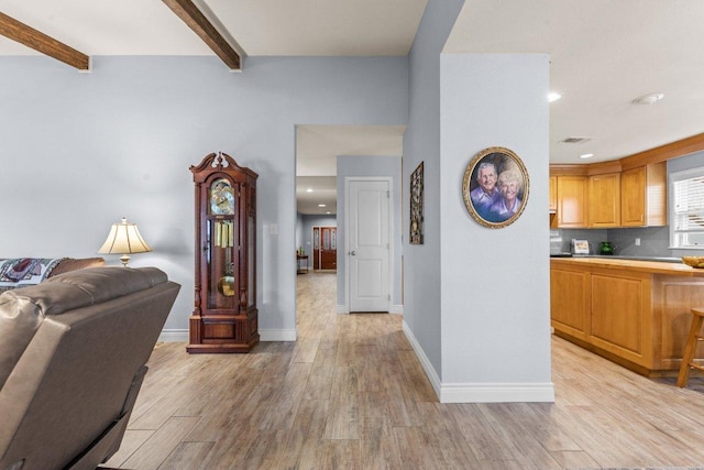 interior space with light wood-type flooring, baseboards, and beam ceiling