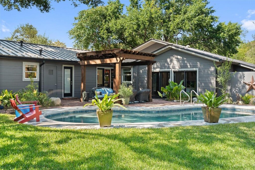 back of house featuring a standing seam roof, a pergola, metal roof, a lawn, and an outdoor pool