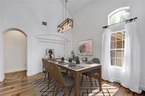 dining area featuring high vaulted ceiling, arched walkways, and wood finished floors