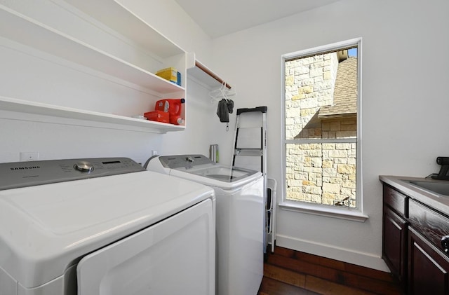 clothes washing area with cabinet space, dark wood-type flooring, a sink, separate washer and dryer, and baseboards