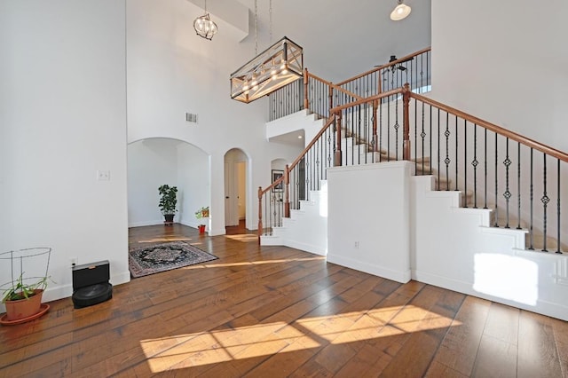 entrance foyer featuring arched walkways, a notable chandelier, visible vents, stairway, and wood-type flooring