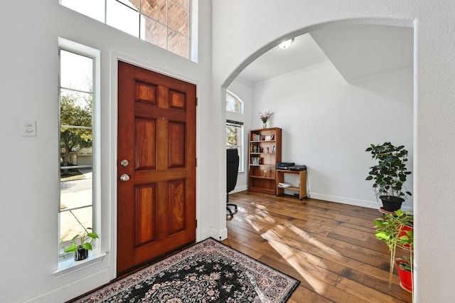 entrance foyer with hardwood / wood-style flooring, baseboards, arched walkways, and ornamental molding