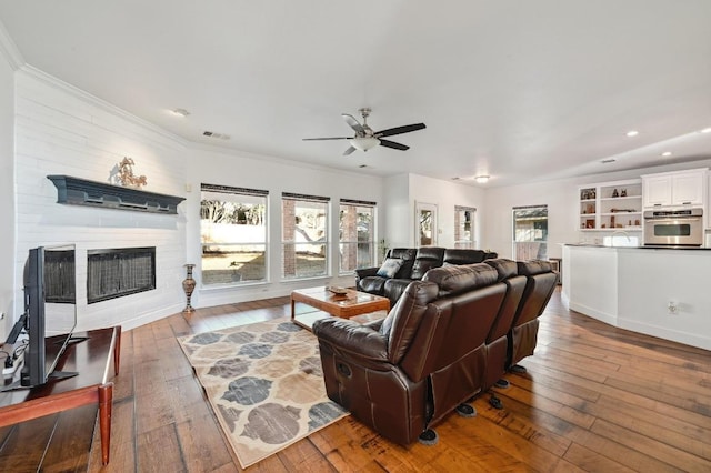 living room with visible vents, a ceiling fan, hardwood / wood-style floors, crown molding, and a fireplace