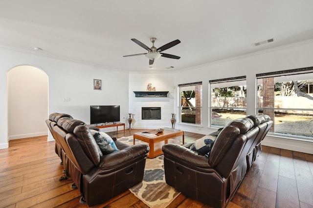 living room with crown molding, arched walkways, hardwood / wood-style floors, and a glass covered fireplace