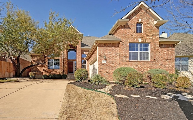 traditional-style home featuring brick siding, roof with shingles, concrete driveway, an attached garage, and fence