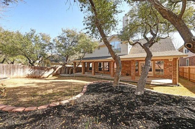 back of property with brick siding, a patio area, a fenced backyard, and a shingled roof