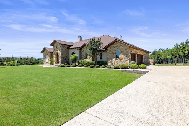 french country home with an attached garage, driveway, stone siding, a chimney, and a front yard