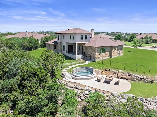 rear view of property featuring stone siding, an in ground hot tub, fence, a yard, and a patio area