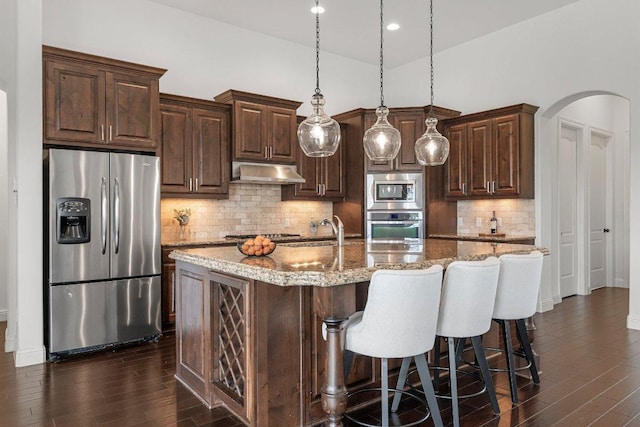 kitchen featuring stainless steel appliances, arched walkways, under cabinet range hood, and dark brown cabinets