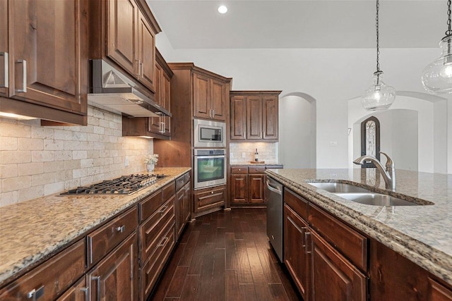 kitchen featuring arched walkways, dark wood-style flooring, appliances with stainless steel finishes, a sink, and under cabinet range hood