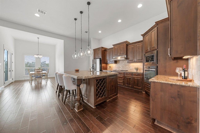 kitchen featuring under cabinet range hood, dark wood-style flooring, visible vents, appliances with stainless steel finishes, and decorative backsplash