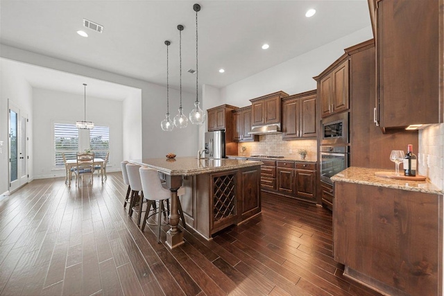 1104 Squaw Vly, Leander, TX 78641 - kitchen featuring stainless steel appliances, under cabinet range hood, decorative backsplash, a kitchen breakfast bar, and light stone countertops