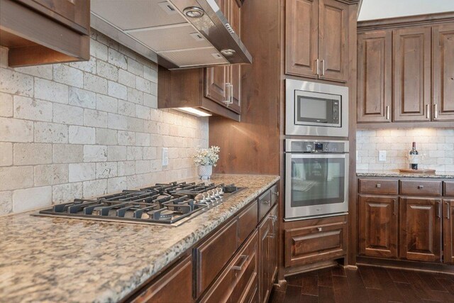 1104 Squaw Vly, Leander, TX 78641 - kitchen with stainless steel appliances, exhaust hood, decorative backsplash, light stone counters, and dark wood finished floors