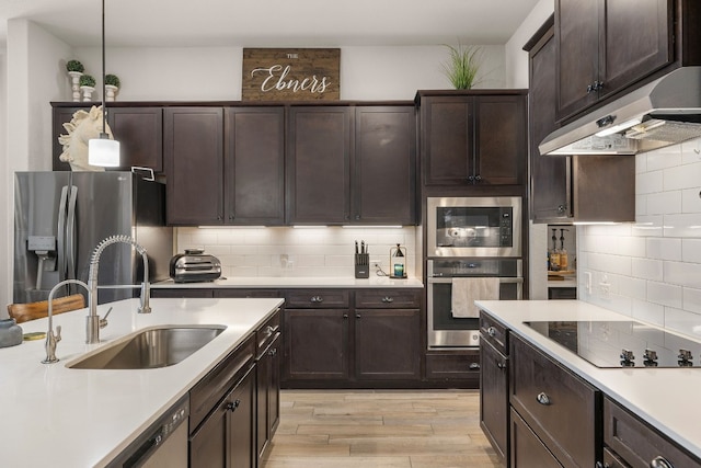 kitchen with stainless steel appliances, light countertops, backsplash, a sink, and under cabinet range hood