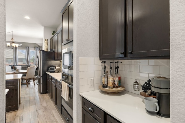 kitchen featuring light wood-style flooring, a notable chandelier, light countertops, appliances with stainless steel finishes, and decorative backsplash