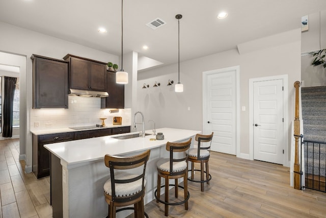 kitchen with visible vents, decorative backsplash, light wood-type flooring, under cabinet range hood, and a sink