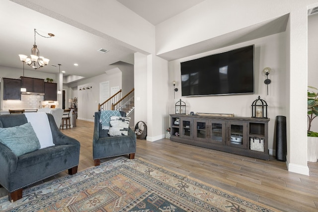 living area with visible vents, light wood-style flooring, a chandelier, baseboards, and stairs