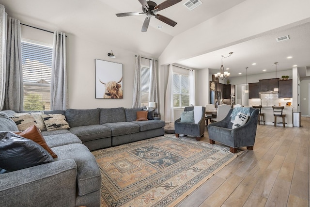 living area featuring vaulted ceiling, light wood finished floors, ceiling fan with notable chandelier, and visible vents