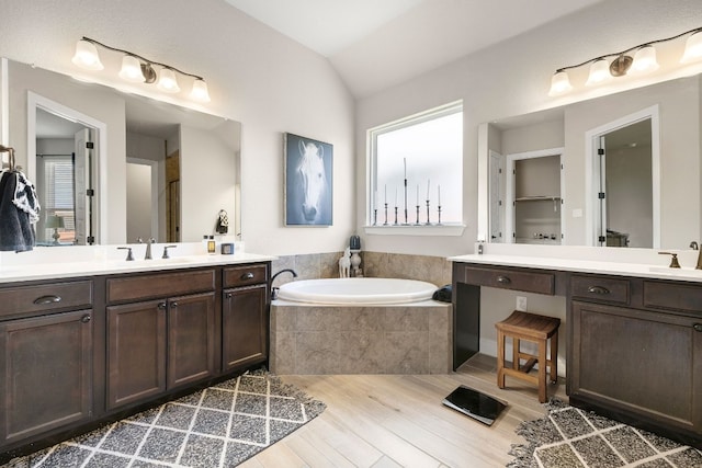 bathroom with a bath, two vanities, vaulted ceiling, and a sink