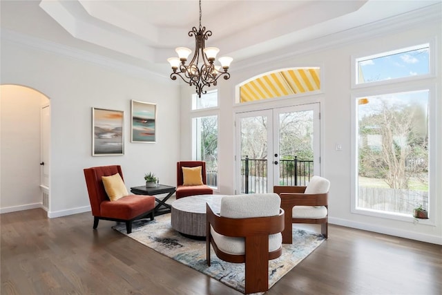 sitting room with arched walkways, a tray ceiling, wood finished floors, and baseboards