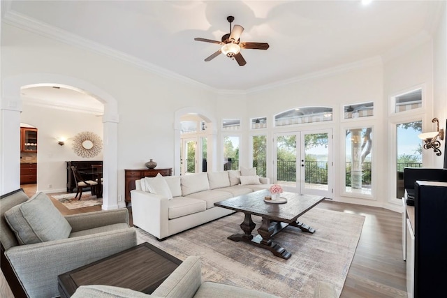 living area featuring crown molding, arched walkways, plenty of natural light, and wood finished floors