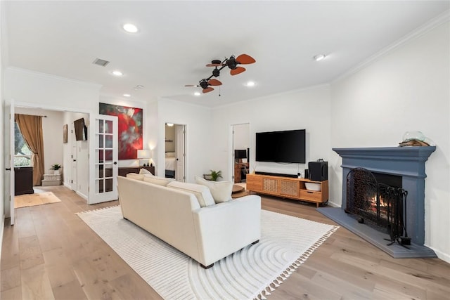 living room with a lit fireplace, light wood-type flooring, visible vents, and crown molding