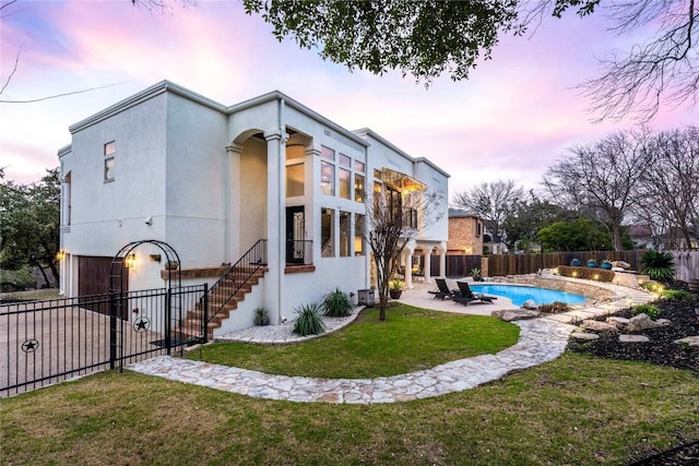 back of property at dusk featuring a fenced in pool, a yard, a patio, stucco siding, and a fenced backyard