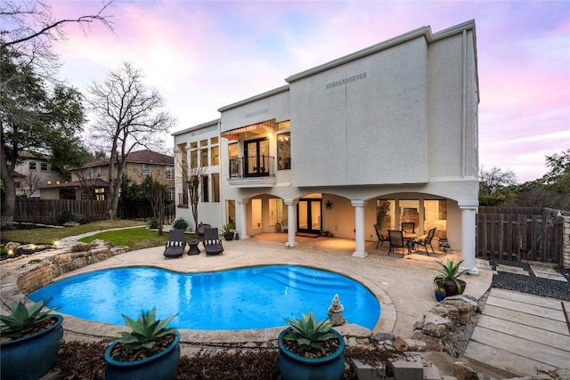 back of property at dusk featuring a fenced in pool, a patio area, stucco siding, and a balcony