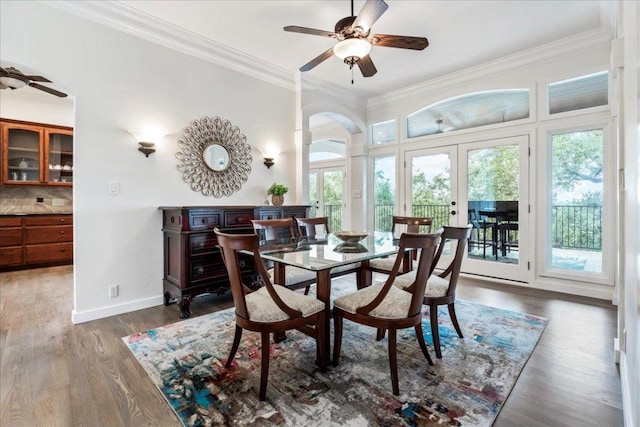 dining space with baseboards, arched walkways, wood finished floors, crown molding, and french doors