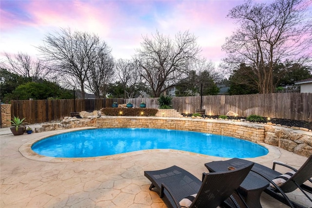 pool at dusk with a patio area, a fenced backyard, and a fenced in pool