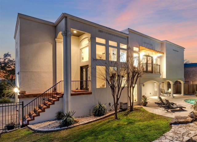 rear view of house featuring a balcony, fence, a patio, and stucco siding