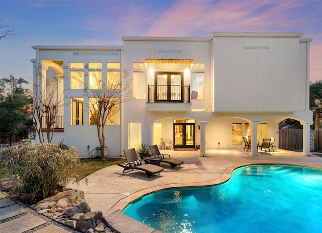 back of house at dusk featuring french doors, a fenced in pool, fence, a balcony, and a patio
