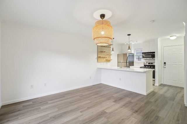 1422 Collier St Unit 102, Austin, TX 78704 - kitchen with appliances with stainless steel finishes, a peninsula, white cabinetry, wood finished floors, and pendant lighting