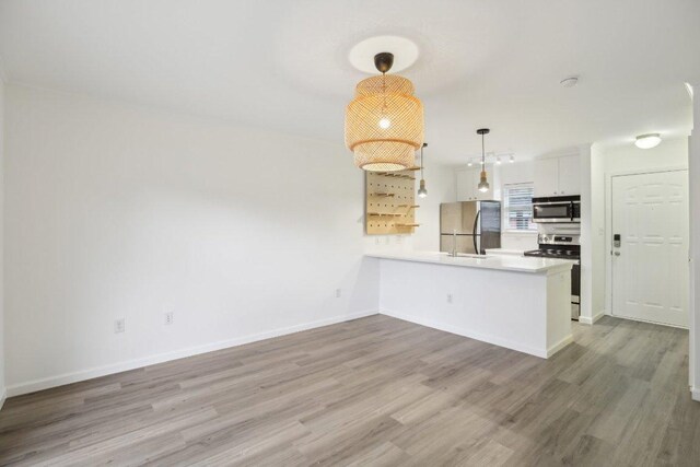 1422 Collier St Unit 102, Austin, TX 78704 - kitchen with appliances with stainless steel finishes, a peninsula, wood finished floors, white cabinets, and decorative light fixtures
