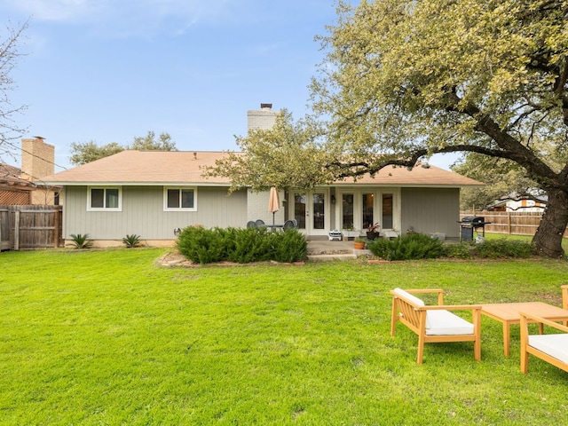 rear view of property with a yard, a chimney, fence, and french doors