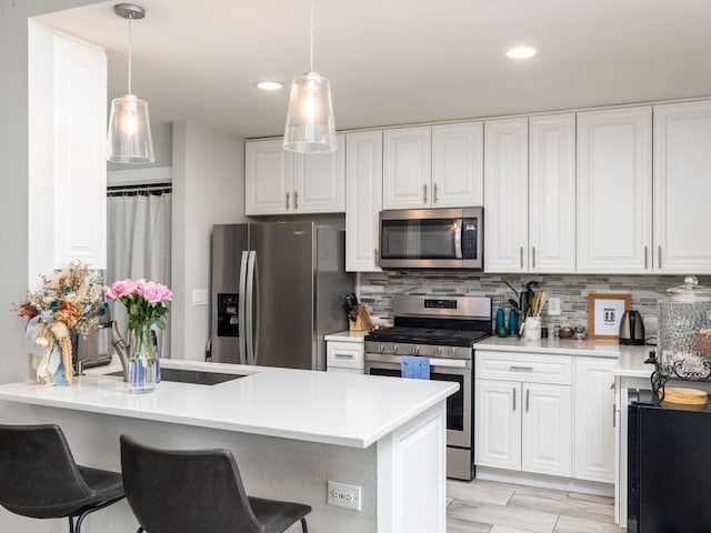 kitchen featuring stainless steel appliances, tasteful backsplash, white cabinets, a peninsula, and a kitchen breakfast bar