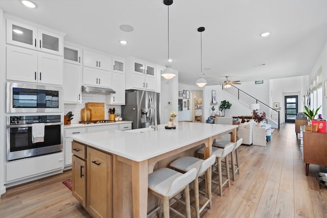 kitchen with under cabinet range hood, stainless steel appliances, a sink, light wood-type flooring, and tasteful backsplash