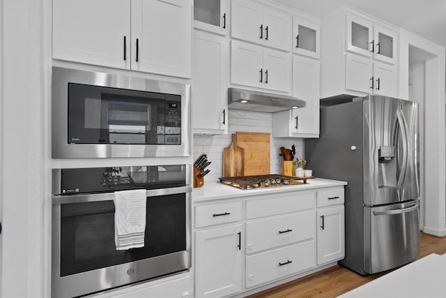 kitchen featuring under cabinet range hood, stainless steel appliances, white cabinetry, light countertops, and tasteful backsplash