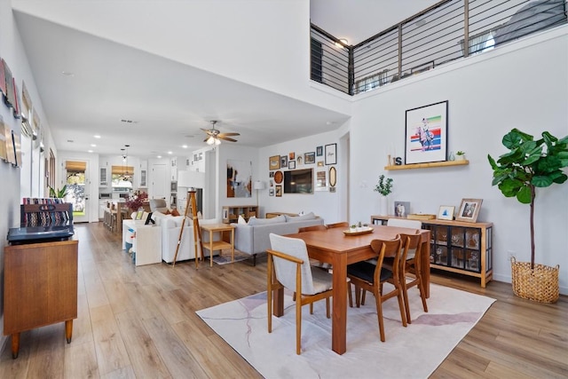 dining room with a towering ceiling, light wood finished floors, ceiling fan, and recessed lighting