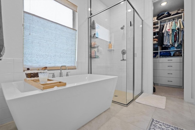 bathroom with a spacious closet, a wealth of natural light, a stall shower, and tile walls