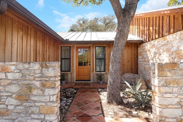 entrance to property featuring stone siding, metal roof, board and batten siding, and a standing seam roof