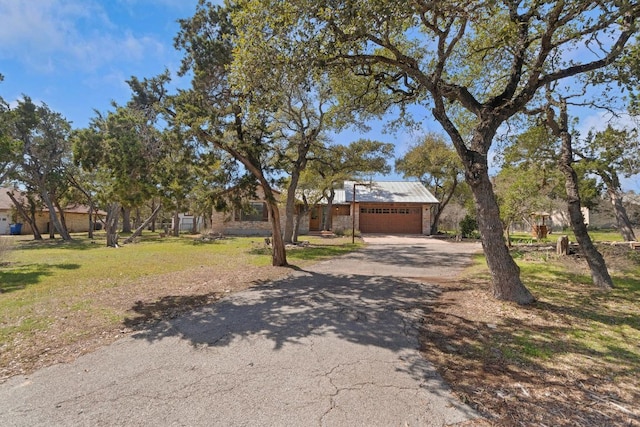 view of front facade with metal roof, aphalt driveway, an attached garage, and a front yard