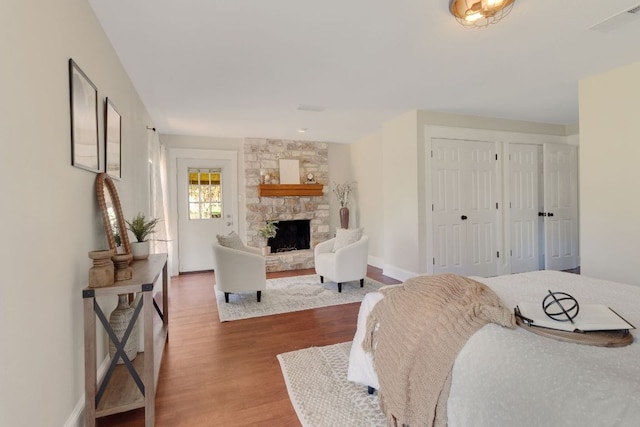 bedroom with baseboards, visible vents, wood finished floors, a stone fireplace, and two closets