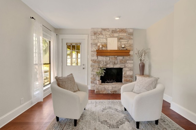 living area featuring a stone fireplace, wood finished floors, and baseboards