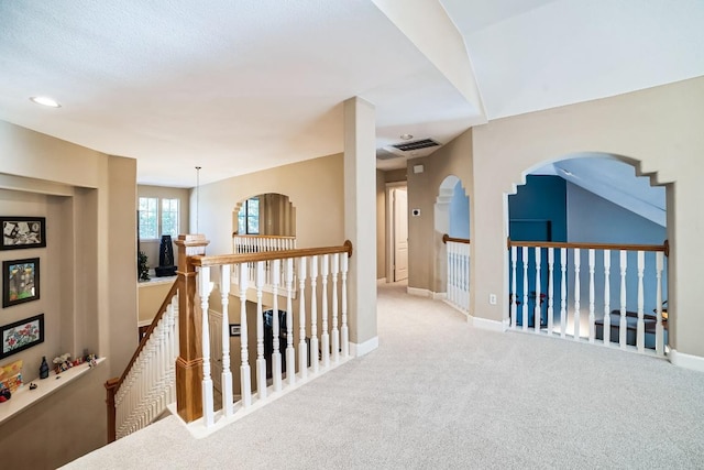 hall featuring carpet, baseboards, visible vents, and an upstairs landing